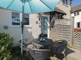 A patio with a round table four chairs umbrella and a bottle on the table at Malting Cottage in Dawlish
