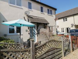 Front of a cottage with a blue door a patio table and umbrella behind a wooden fence at Malting Cottage in Dawlish