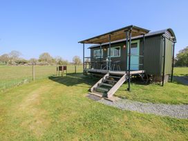 A shepherds hut with a covered porch and stairs in a grassy fenced field at Gilberry Shepherds Hut in Wall under Heywood near Church Stretton