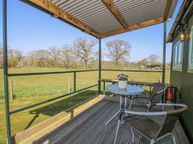 An outdoor seating area with two chairs a small table and a potted plant overlooking a grassy field at Gilberry Shepherds Hut in Wall under Heywood near Church Stretton