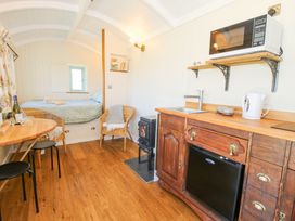 A compact living space with a bed in the background wicker chairs a small stove a wooden kitchen unit with a sink kettle microwave and a table with chairs at Gilberry Shepherds Hut Wall under Heywood near Church Stretton