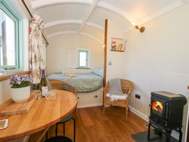 A small room with a bed towels wicker chairs a wood stove and a wooden table with wine at Gilberry Shepherds Hut Wall under Heywood near Church Stretton