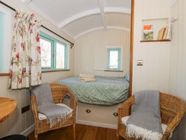 A small bedroom with a bed folded towels two wicker chairs with blankets and floral curtains at Gilberry Shepherds Hut in Wall under Heywood near Church Stretton