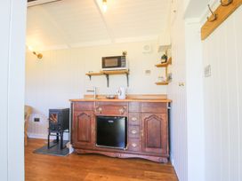 A kitchenette with wooden cabinets a microwave on a shelf a kettle and a small stove at Gilberry Shepherds Hut Wall under Heywood near Church Stretton
