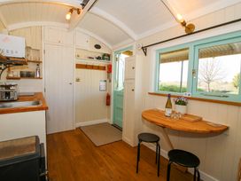 A small kitchen area with a sink, toaster, microwave and shelves next to a wooden fold-down table with two stools at Gilberry Shepherds Hut Wall under Heywood near Church Stretton