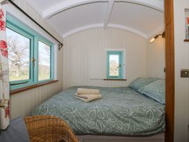 A small bedroom with a bed covered in green floral bedding folded towels on the bed a wicker chair and blue framed windows at Gilberry Shepherds Hut Wall under Heywood near Church Stretton
