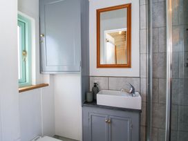 A bathroom with a grey cabinet and sink a mirror above and a turquoise window at Gilberry Shepherds Hut Wall under Heywood near Church Stretton