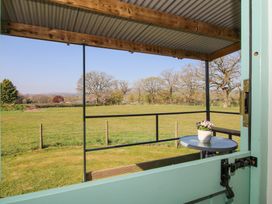 A porch with a table and a flower pot overlooking a fenced grassy field with trees at Gilberry Shepherds Hut in Wall under Heywood near Church Stretton