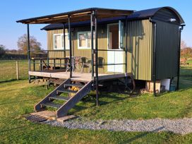 A green shepherds hut with a covered porch and metal chairs in a grassy field at Gilberry Shepherds Hut Wall under Heywood near Church Stretton