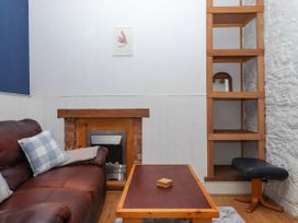 A seating area with a brown leather sofa and cushions a wooden coffee table a fireplace and wooden shelving against a white wall at Harbour Hideaway in Dartmouth