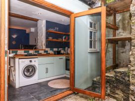 A kitchen with a washing machine sink shelves and blue tiled backsplash with an open glass door to a stone outdoor area at Harbour Hideaway in Dartmouth
