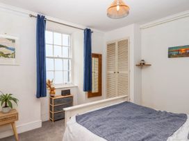 A bedroom with a bed covered by a gray blanket a window with blue curtains a small dresser and a wooden side table with a plant at Harbour Hideaway in Dartmouth