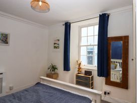 A bedroom with a bed covered with a blue blanket a window with blue curtains a wooden framed mirror and small wooden cabinets at Harbour Hideaway Dartmouth