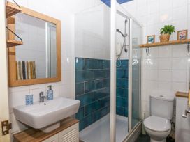 A bathroom with a sink mirror shower with blue tiles and a toilet with shelf holding plant and pictures at Harbour Hideaway in Dartmouth