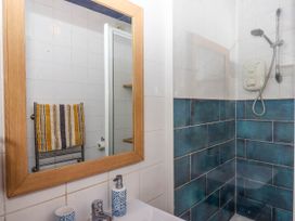 A bathroom with a wooden framed mirror a sink with a tap and soap dispenser a shower area with blue tiles and a striped towel on a rail at Harbour Hideaway in Dartmouth