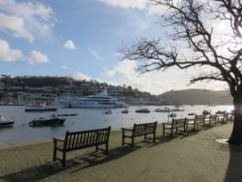 A waterfront area with benches along a paved path boats in the water and houses on a hillside at Harbour Hideaway in Dartmouth