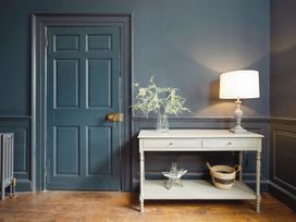 A blue paneled door next to a white table with a lamp vase with flowers and decorative items on a wooden floor at Holmer House Farm in Holmer near Hereford