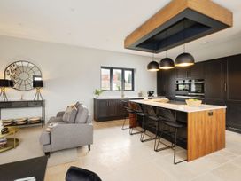 A kitchen with a wooden island and black stools next to a grey sofa and a console table with lamps and a round mirror at Holmer House Farm in Holmer near Hereford