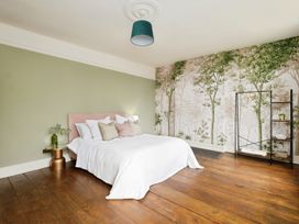 A bedroom with a large bed featuring multiple pillows a side table with a green vase hardwood floor a tree mural on one wall and a clothes rack at Holmer House Farm in Holmer near Hereford