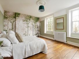 A bedroom with a bed covered in white bedding next to two windows and a wall with tree wallpaper at Holmer House Farm in Holmer near Hereford
