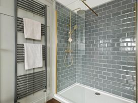 A bathroom shower area with grey subway tile walls gold shower fixtures and a black towel radiator with white towels at Holmer House Farm in Holmer near Hereford
