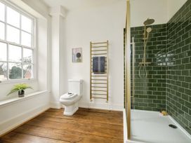 A bathroom with a toilet a gold towel rack a shower with green tiles and a window with a plant on the sill at Holmer House Farm in Holmer near Hereford