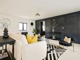 A living room with a beige sofa and yellow pillows a black armchair a black console table and a black and white rug at Holmer House Farm in Holmer near Hereford