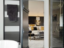 A bathroom with a towel on a black heated towel rail and a shower visible through a glass door with a view into a living room with a white sofa and yellow cushions at Holmer House Farm in Holmer near Hereford