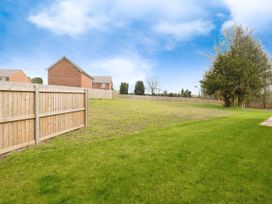 A fenced grassy backyard with trees and neighboring brick houses at Holmer House Farm in Holmer near Hereford