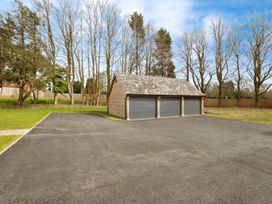 A detached triple garage with closed doors surrounded by trees and a driveway at Holmer House Farm in Holmer near Hereford