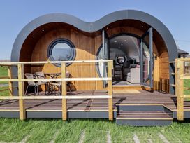 A wooden pod with curved roof and circular windows with a deck and outdoor seating at The Hazel Pod in Cowbridge
