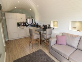 An open plan living room and kitchen with two chairs at a breakfast bar and a sofa with a cushion at The Hazel Pod in Cowbridge