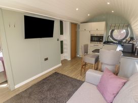 A living area with a sofa and purple pillow a wall-mounted TV a small kitchen with appliances and a round window at The Hazel Pod in Cowbridge