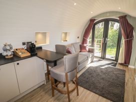 A room with a gray sofa, two gray chairs, a small table, coffee machine, and double glass doors with maroon curtains at The Hazel Pod in Cowbridge