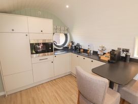 A kitchen with built in cabinets a microwave a round window a black countertop appliances and two chairs at The Hazel Pod in Cowbridge