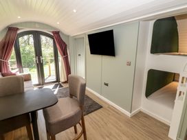 A small living area with a table and chairs a sofa bunk beds and a wall-mounted TV near glass doors with red curtains at The Hazel Pod in Cowbridge