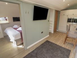 A living area with a wall-mounted TV and a kitchen area visible with cabinets and a microwave at The Hazel Pod in Cowbridge