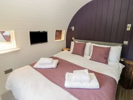 A bedroom with a double bed white and purple bedding towels on bed and a wall-mounted TV at The Hazel Pod in Cowbridge