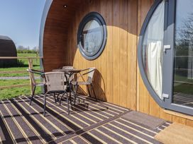 An outdoor patio with a round table and four chairs next to a wooden pod with round windows at The Hazel Pod in Cowbridge