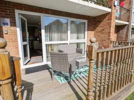 A small outdoor seating area with two wicker chairs and a glass-top table on a wooden deck at 98 Waterside Park in Corton