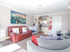 A living room with a red leather sofa, three armchairs, a small round table, and an open kitchen at 98 Waterside Park in Corton