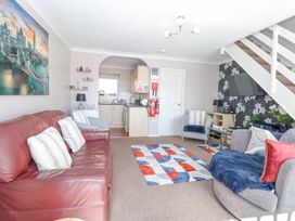A living room with a red leather sofa, two armchairs, a patterned rug, a wall-mounted TV, and a view into a kitchen at 98 Waterside Park in Corton