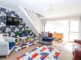 A living room with a round chair a glass coffee table a wall-mounted TV floral wallpaper and a colorful rug at 98 Waterside Park in Corton