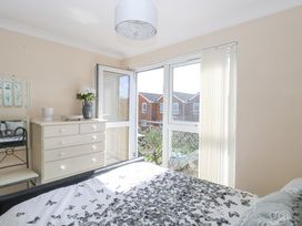 A bedroom with a bed, white dresser with decorations, chair, and glass door leading to a balcony at 98 Waterside Park in Corton