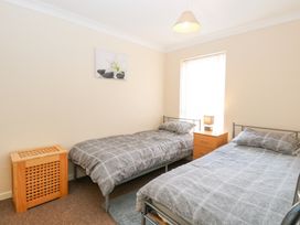 A bedroom with two single beds a wooden nightstand with a lamp a wooden laundry basket and a flower picture on the wall at 98 Waterside Park in Corton