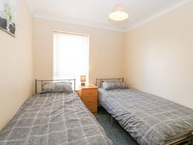 A bedroom with two single beds each with gray bedding a wooden nightstand with a lamp between the beds and a window with vertical blinds at 98 Waterside Park in Corton