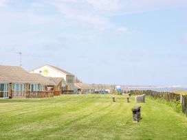 A grassy area with wooden benches near seaside cottages and a wooden fence at 98 Waterside Park in Corton