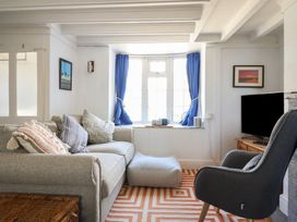 A living room with a gray sofa and striped cushions a dark gray armchair a flat screen tv on a wooden stand and blue curtains at Glan Y Mor Borth in Borth
