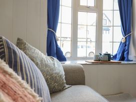 A sofa with patterned cushions near a window with blue curtains and a tea set on the windowsill at Glan Y Mor Borth in Borth