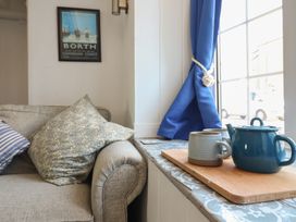 A sofa with patterned and striped cushions and a teapot with mugs on a wooden board by a window with blue curtains at Glan Y Mor Borth in Borth